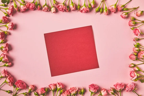 Vue du dessus du cadre faite de belles roses roses et carte blanche sur rose — Photo de stock
