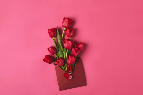 Vue du dessus des tulipes rouges dans l'enveloppe sur rose, concept de fête des mères — Photo de stock