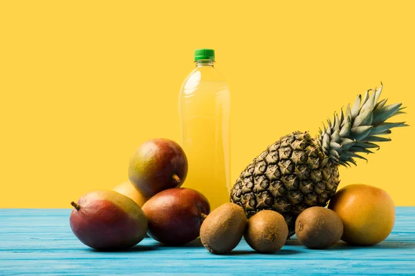 Frutas tropicais maduras frescas e bebida frutada natural em garrafa de plástico em mesa de madeira turquesa — Fotografia de Stock