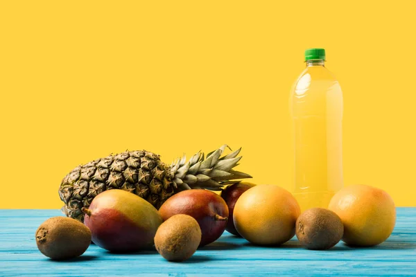 Close-up view of fresh ripe tropical fruits and natural fruity drink in plastic bottle on yellow — Stock Photo