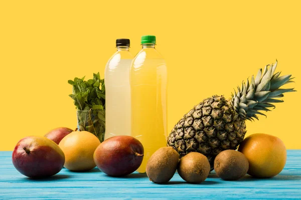 Boissons fruitées en bouteilles en plastique et fruits tropicaux frais mûrs sur plateau en bois turquoise — Photo de stock