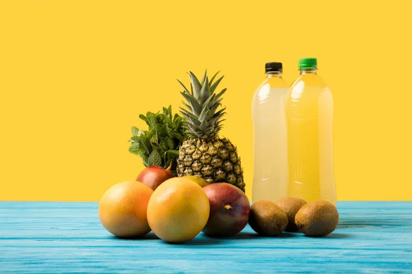 Vue rapprochée des boissons fruitées dans des bouteilles en plastique et des fruits tropicaux frais mûrs sur jaune — Photo de stock