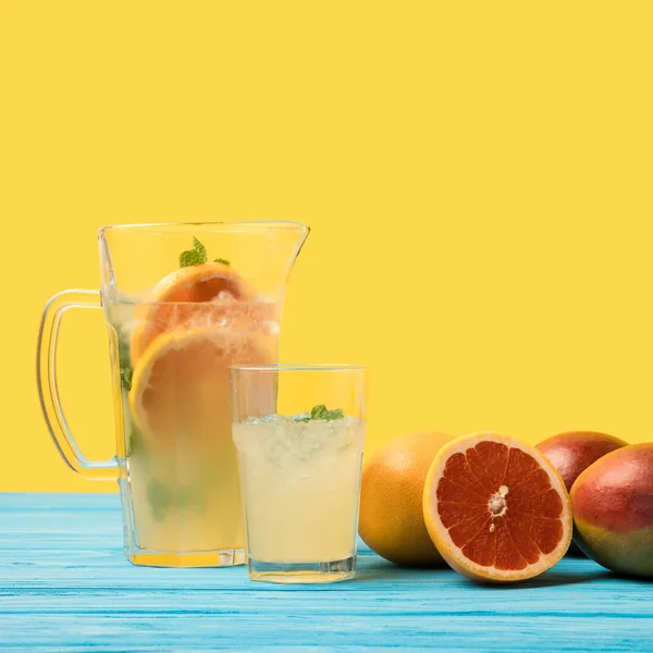 Vista de cerca de mangos frescos con pomelos y bebida fría de verano en vaso y jarra en amarillo - foto de stock
