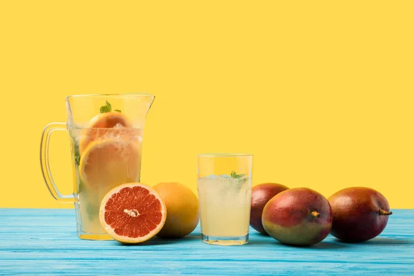 Fresh mangoes with grapefruits and cold summer drink in glass and jug on turquoise wooden table top — Stock Photo