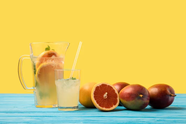 Frutas tropicales maduras frescas y cóctel frío de verano en vaso y jarra sobre mesa de madera turquesa - foto de stock