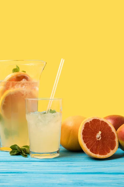 Vista de cerca de frutas tropicales frescas maduras y cóctel frío de verano en vaso y jarra en amarillo - foto de stock