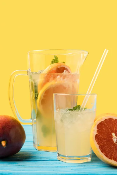 Vista close-up de manga madura fresca, toranja fatiada e bebida fria de verão em vidro e jarro em amarelo — Fotografia de Stock