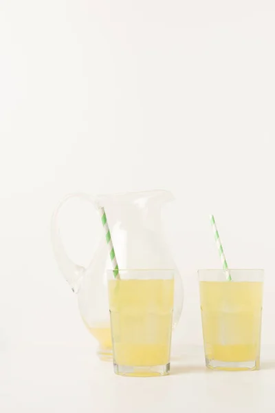 Close-up view of glasses with straws and glass jug with fresh tropical juice on grey — Stock Photo