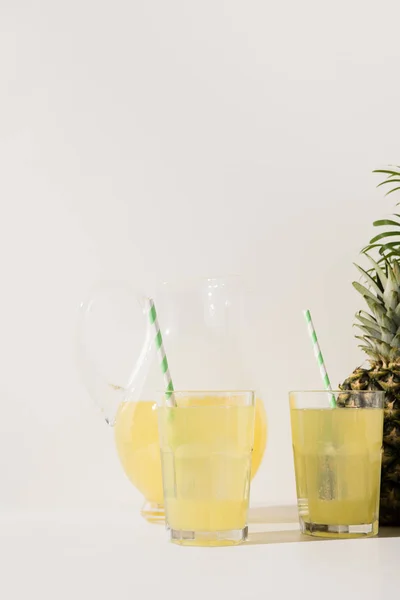 Vista de cerca de vasos y jarra de vidrio con jugo fresco y piña madura en gris - foto de stock