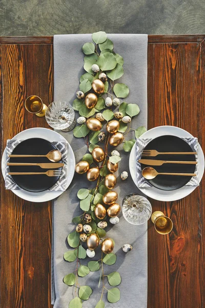 Верхний вид пасхальных золотых яиц, тарелок и посуды на праздничный стол в ресторане — стоковое фото