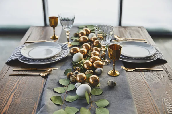 Ovos dourados de Páscoa, pratos e copos na mesa — Fotografia de Stock