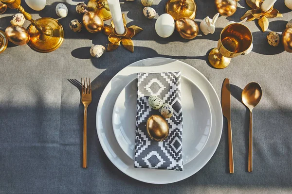 Вид на золотое яйцо и перепелиные яйца на тарелках в ресторане, пасхальная концепция — Stock Photo