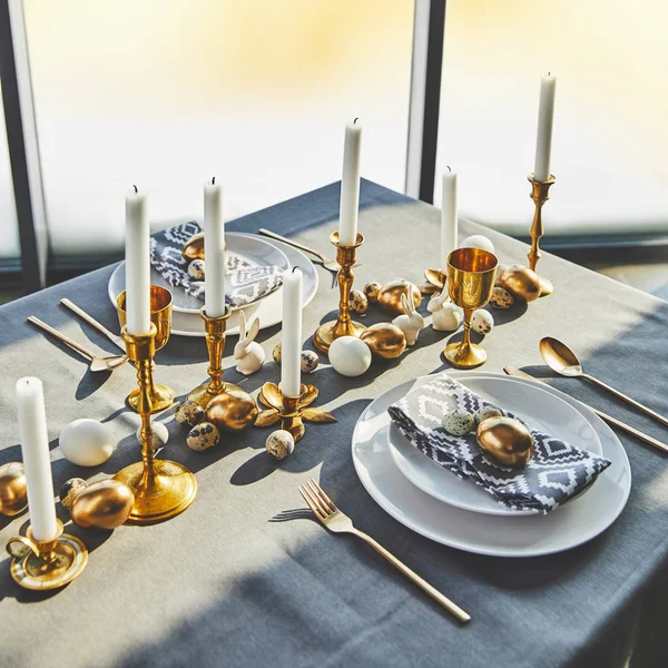 Vista en ángulo alto de los huevos de Pascua y velas en la mesa festiva con luz solar - foto de stock