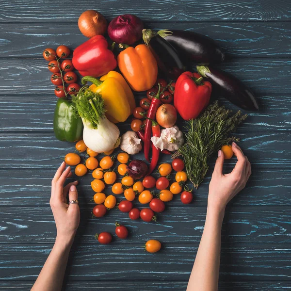 Imagen recortada de la mujer tomando verduras orgánicas maduras de mesa de madera - foto de stock