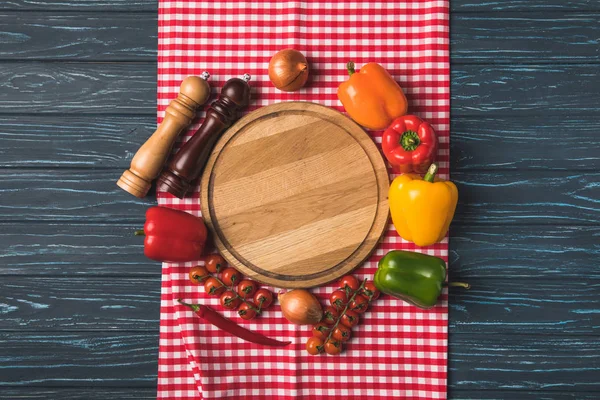 Vista superior de verduras orgánicas maduras y molinillos de pimienta alrededor de tablero de madera en la mesa - foto de stock