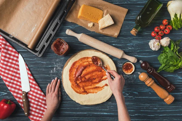 Image recadrée de la femme mettant des pâtes à la tomate sur la pâte pour pizza — Photo de stock