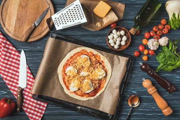 Blick von oben auf ungekochte Pizza auf Tablett auf Tisch in Küche — Stockfoto