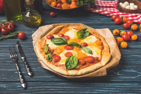 Apetitosa pizza sabrosa con tomates cherry y albahaca en la mesa — Stock Photo
