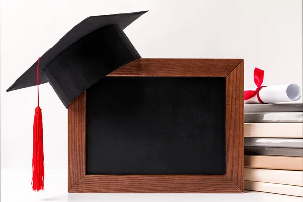 Diploma on stack of books, empty blackboard with academic cup isolated on white — Stock Photo