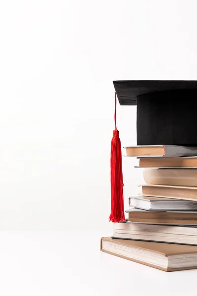 Chapéu acadêmico na pilha de livros isolados em branco — Fotografia de Stock