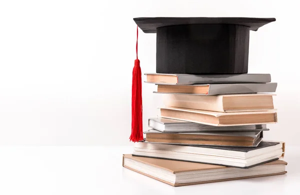 Квадратная академическая шляпа на стопке разных книг, изолированных на белом — стоковое фото
