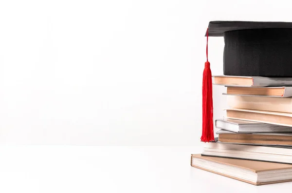 Vista recortada de quare acadêmico cap na pilha de diferentes livros isolados em branco — Fotografia de Stock