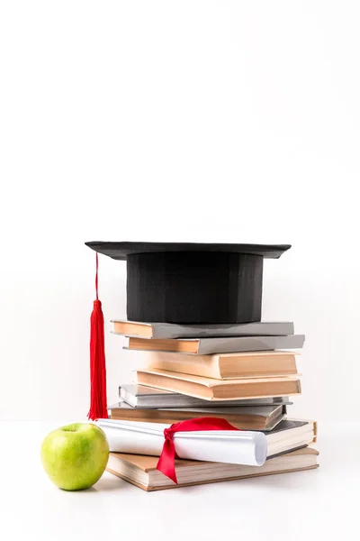 Montón de libros con sombrero académico, diploma y manzana aislados en blanco - foto de stock