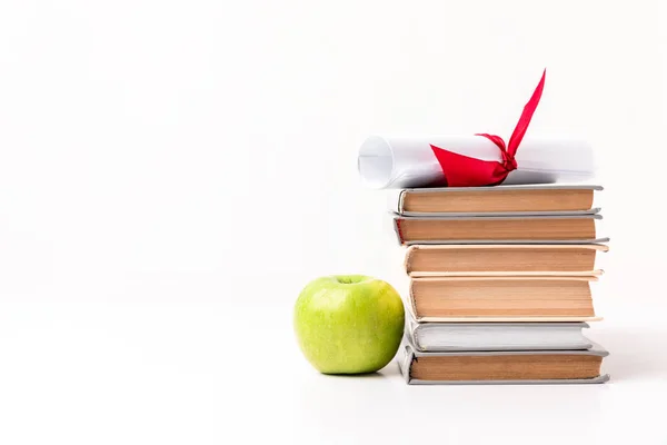 Apple near pile of books with diploma on top isolated on white — Stock Photo