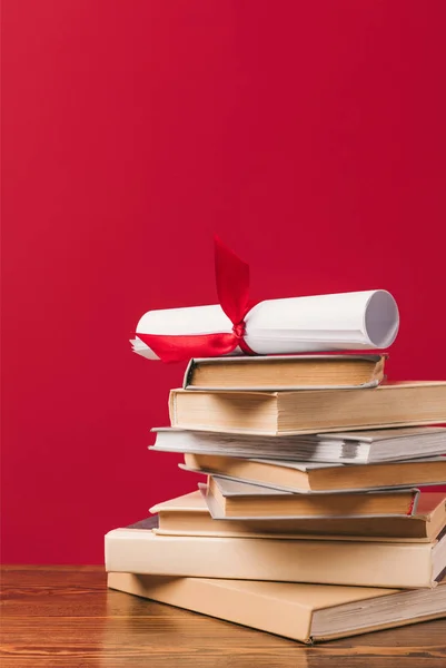 Diploma on top of stack of books on red — Stock Photo