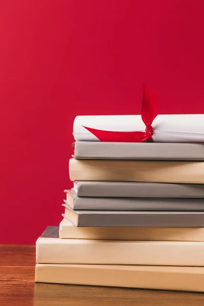 Cropped image of diploma on top of stack of books on red — Stock Photo