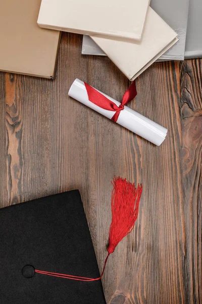 Vista superior de libros, diploma y tapa académica sobre fondo de madera - foto de stock