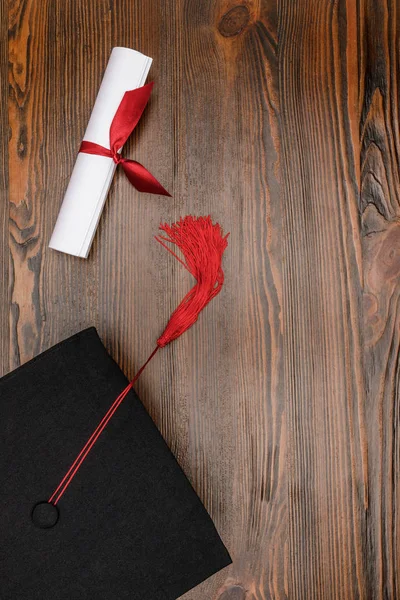 Vista dall'alto del diploma e cappello accademico quadrato su sfondo legno — Foto stock