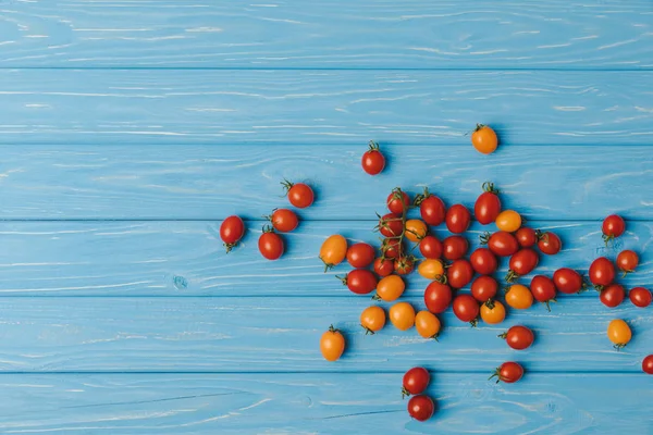 Vista superior de tomates cherry rojos y anaranjados sobre mesa azul - foto de stock