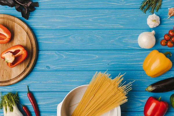 Vista elevada de las pastas y verduras sin cocer sobre la mesa azul - foto de stock