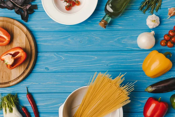 Вид зверху на неварені макарони та овочі на синьому столі — стокове фото