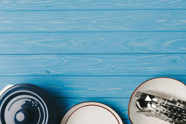 Верхний вид тарелок, сковороды и посуды на синий стол — стоковое фото