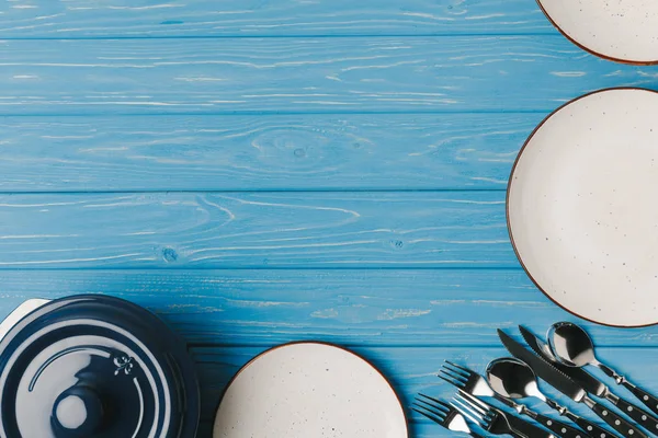 Top view of plates, utensil and pan on blue table — Stock Photo