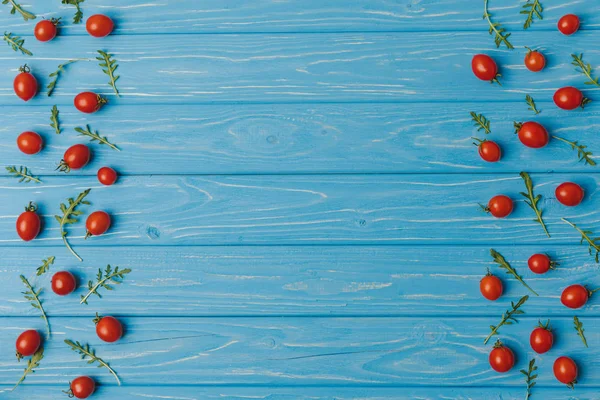 Верхний вид помидоров черри с рукколой на голубом столе — стоковое фото
