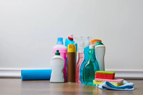 Different bottles with domestic supplies for spring cleaning on wooden floor — Stock Photo