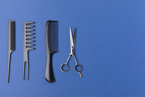 Deitado plano com escovas de cabelo pretas e tesoura, isolado em azul — Fotografia de Stock