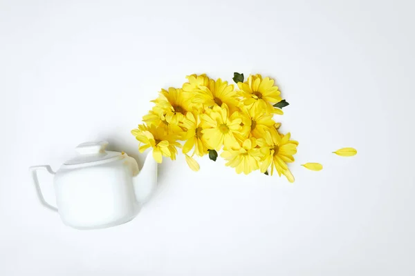 Despejando margaridas amarelas de bule branco isolado em branco — Fotografia de Stock