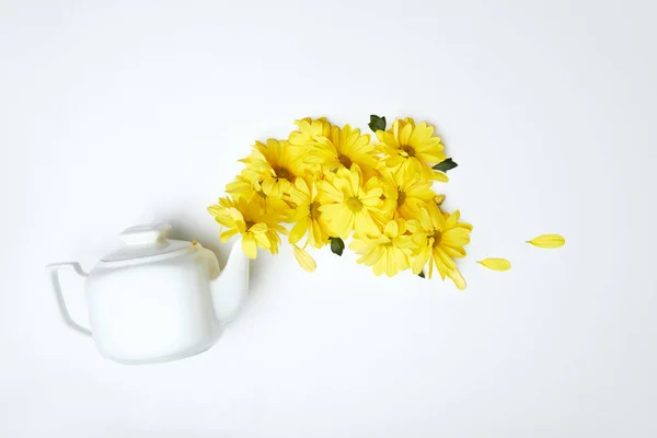 Verser des marguerites jaunes de théière blanche isolée sur blanc — Photo de stock