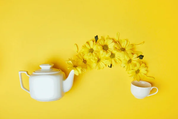 Yellow chrysanthemums pouring into cup from white pot isolated on yellow — Stock Photo