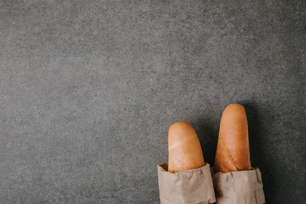 Top view of fresh tasty baguettes in paper bags on grey background — Stock Photo