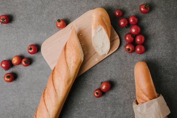 Top view of baguettes, wooden board and fresh tomatoes on grey — Stock Photo