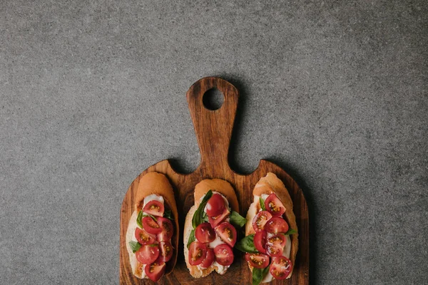 Top view of gourmet italian bruschetta on wooden cutting board on grey — Stock Photo