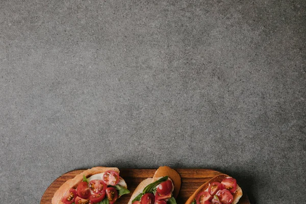 Draufsicht auf köstliche italienische Bruschetta auf Holzbrett auf grauem Hintergrund — Stockfoto