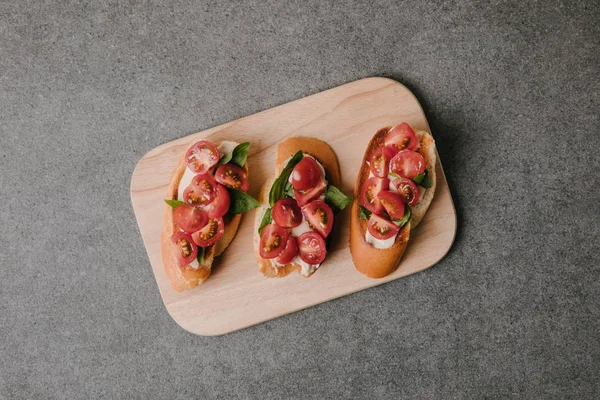 Vue de dessus de bruschetta italienne gourmande sur planche de bois sur gris — Photo de stock