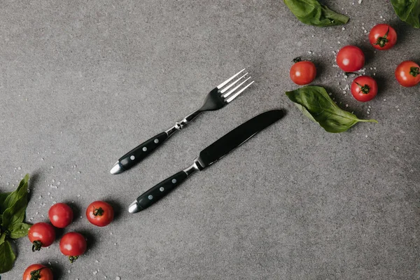 Top view of fresh tomatoes, basil and salt with cutlery on grey — Stock Photo