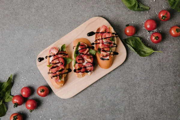 Vue de dessus de la bruschetta italienne traditionnelle sur panneau de bois avec basilic et tomates fraîches sur gris — Photo de stock